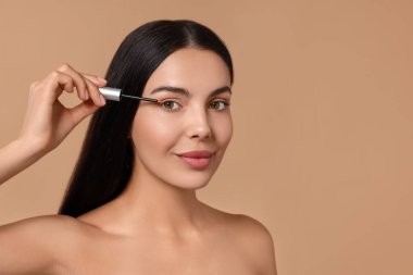 Güzel bir kadın kirpiklerine bej arka plan serumu sürüyor, mesaj için yer var. Kozmetik ürünü