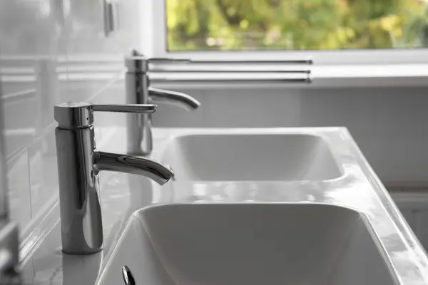 White clean sinks with water taps in bathroom, closeup