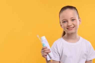 Sarı arka planda elektrikli diş fırçası ve bir tüp diş macunu tutan mutlu kız. Metin için boşluk