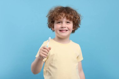 Açık mavi arka planda plastik diş fırçası tutan sevimli küçük çocuk.