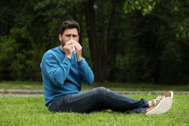 Parktaki yeşil çimlerde mevsimlik bahar alerjisi olan bir adam