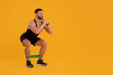 Young man exercising with elastic resistance band on orange background. Space for text clipart