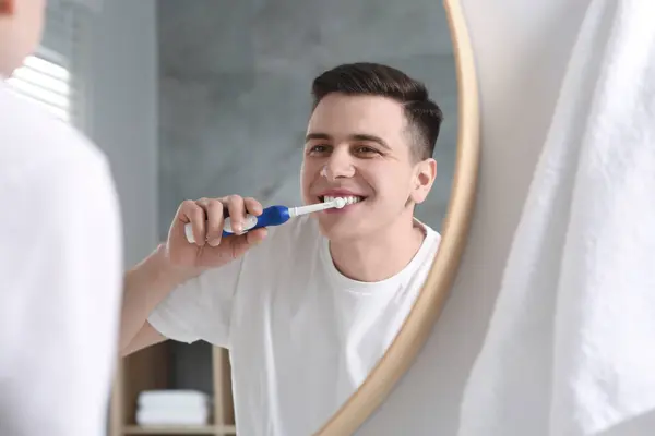 バスルームの鏡の近くに電気歯ブラシで歯を磨く男 — ストック写真