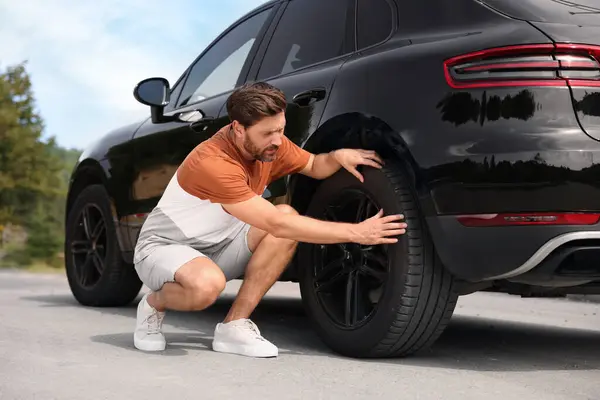 Tire puncture. Man checking wheel of car on roadside outdoors