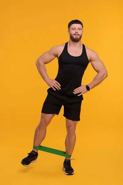 Genç Adam Turuncu Arka Planda Elastik Direnç Bandıyla Egzersiz Yapıyor — Stok fotoğraf
