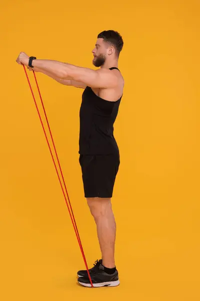 Młody Mężczyzna Ćwiczący Elastyczną Taśmą Oporową Pomarańczowym Tle — Zdjęcie stockowe