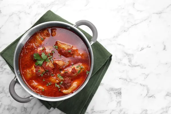 Delicious stuffed cabbage rolls cooked with homemade tomato sauce in pot on white marble table, top view. Space for text
