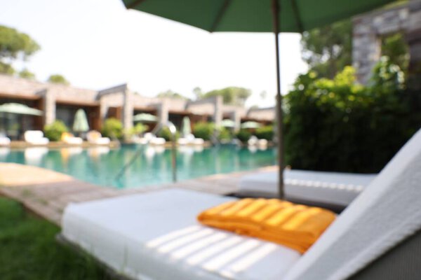 Sunbeds near swimming pool at luxury resort, blurred view
