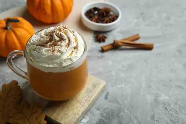 Cup of pumpkin spice latte with whipped cream on light grey table, closeup. Space for text