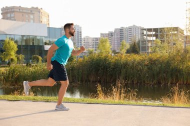 Genç adam parkta göletin yanında koşuyor. Metin için boşluk