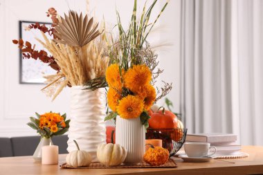 Parlak turuncu çiçekler, balkabakları ve odasındaki ahşap masada yanan mumlarla güzel bir sonbahar kompozisyonu.