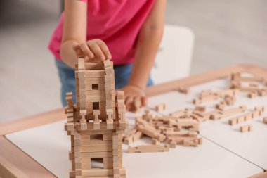 Küçük kız kapalı bir masada tahta kuleyle oynuyor, yakın plan. Çocuk oyuncağı