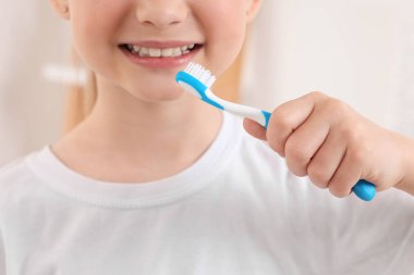 Kapalı mekanda plastik diş fırçası tutan küçük bir kız.