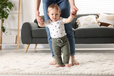 Anne, bebeğine evde halıda yürümeyi öğrenirken bakıyor.