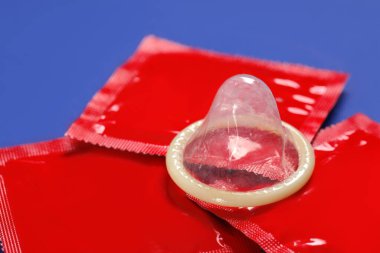 Mavi arka planda paketsiz prezervatif ve paketler, yakın plan. Güvenli seks.