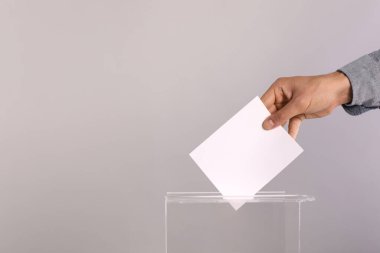 Adam oyunu açık gri arka planda oy sandığına koyuyor, yakın plan. Metin için boşluk
