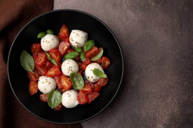 Domatesli Caprese salatası, mozzarella topları ve kahverengi sehpada fesleğen. Metin için boşluk