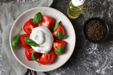 Domatesli, fesleğenli, yağlı ve biberli leziz burata peyniri gri masada, düz yerde.