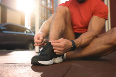 Güneşli bir günde spor salonunda antrenmandan önce ayakkabı bağı bağlayan adam, yakın çekim.