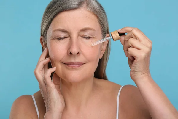 Seniorin Trägt Kosmetikprodukt Auf Ihre Alternde Haut Vor Hellblauem Hintergrund — Stockfoto