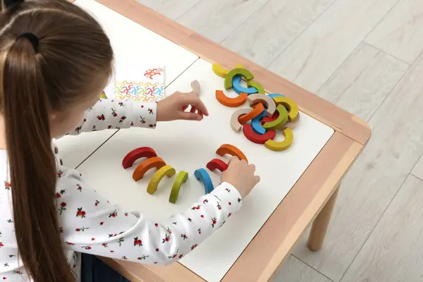 Motor skills development. Girl playing with colorful wooden arcs at white table indoors, above view