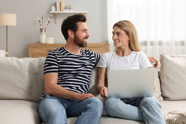 Happy couple with laptop on sofa at home