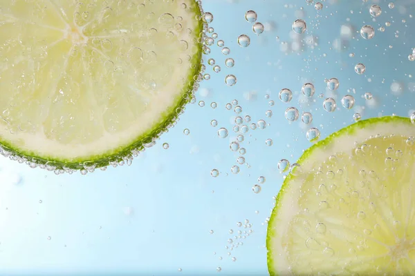 Juicy lime slices in soda water against light blue background, closeup
