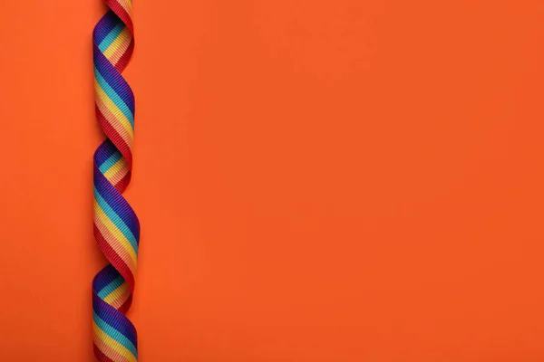 Rainbow ribbon on orange background, top view with space for text. LGBT pride