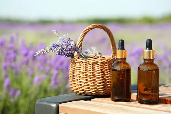 Bottles Essential Oil Wicker Bag Lavender Flowers Wooden Table Field — Stock Photo, Image