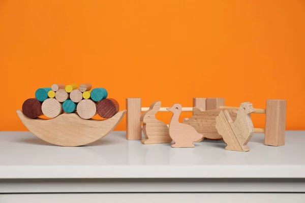Wooden balance toy, animals and fence on white chest of drawers near orange wall, space for text. Children's development
