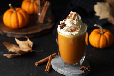 Bir bardak balkabağı aromalı latte. Krem şantili ve siyah masa malzemeli.