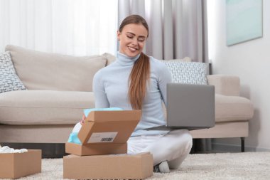 Evde dizüstü bilgisayarı olan mutlu kadın paketleri açıyor. Çevrimiçi mağaza