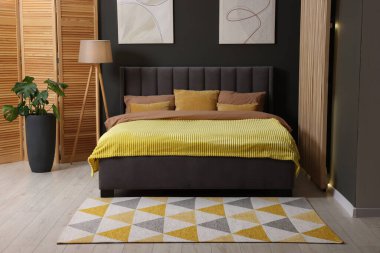 Şık bir odada büyük, rahat bir yatak, lamba ve yeşil bir saksı. Yatak odasının içi.