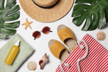 Beyaz zemin üzerinde çanta, yeşil yapraklar ve diğer plaj aksesuarları ile düz kompozisyon yatıyordu