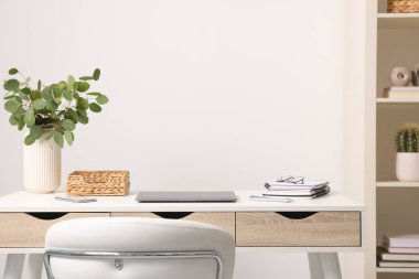 Merkez ofis. Laptop, bardaklar, kırtasiye malzemeleri ve içerideki beyaz masanın üzerine bitki. Metin için boşluk