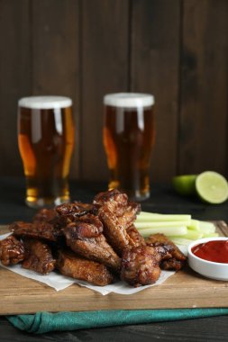 Lezzetli tavuk kanatları, siyah ahşap masada bira ile servis edilir.