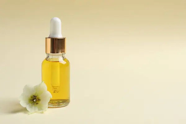 Bottle with cosmetic oil and flower on beige background. Space for text