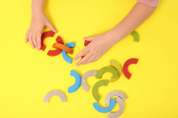 Motor skills development. Girl playing with colorful wooden arcs at yellow table, top view