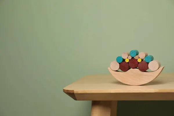 Wooden balance toy on table near olive wall, space for text. Children's development