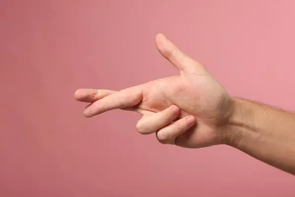 Man crossing his fingers on pink background, closeup