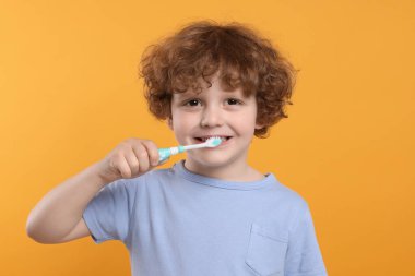 Sevimli küçük çocuk sarı arka planda plastik diş fırçasıyla dişlerini fırçalıyor.