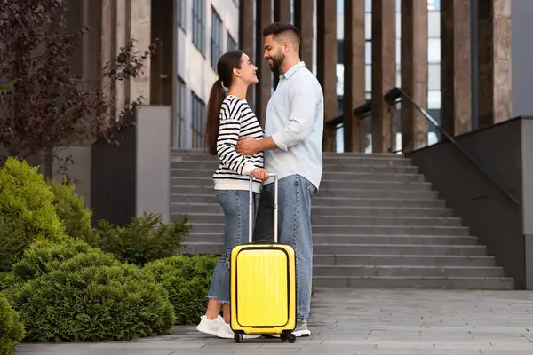 stock image Long-distance relationship. Beautiful young couple with suitcase near building outdoors