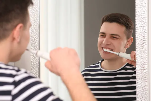 バスルームの鏡の近くに電気歯ブラシで歯を磨く男 — ストック写真