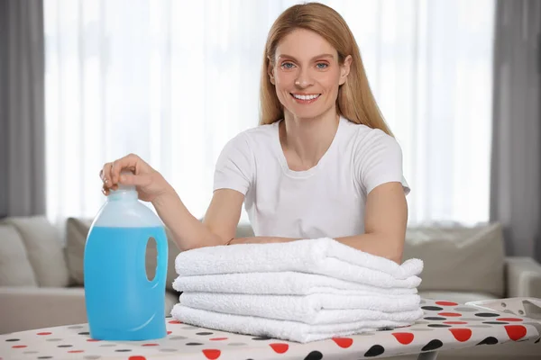 Woman with fabric softener and clean towels in room, space for text