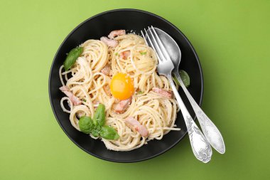 Yumurta sarısı ve açık yeşil arka planda çatal bıçaklı Carbonara makarnası.