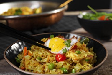 Lezzetli pirinçli yemek çubuklarıyla yumurta, ahşap masada et ve sebzeler, yakın plan.