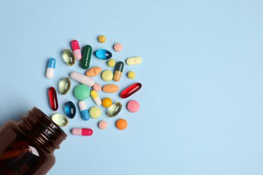 Açık mavi arka planda bir sürü farklı hap içeren plastik tıbbi şişe, düz. Metin için boşluk