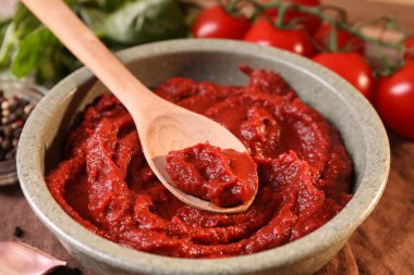 Bir kase lezzetli domates ezmesi, kaşıkla ve malzemelerle birlikte, yakın plan.