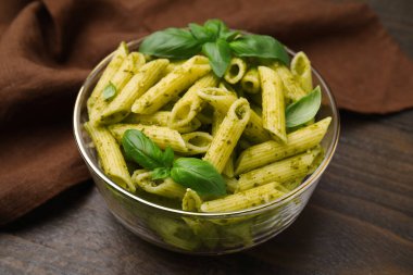 Pesto soslu lezzetli makarna ve ahşap masada fesleğen, yakın plan.