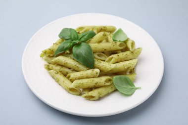 Pesto soslu lezzetli makarna ve açık gri arka planda fesleğen, yakın plan.